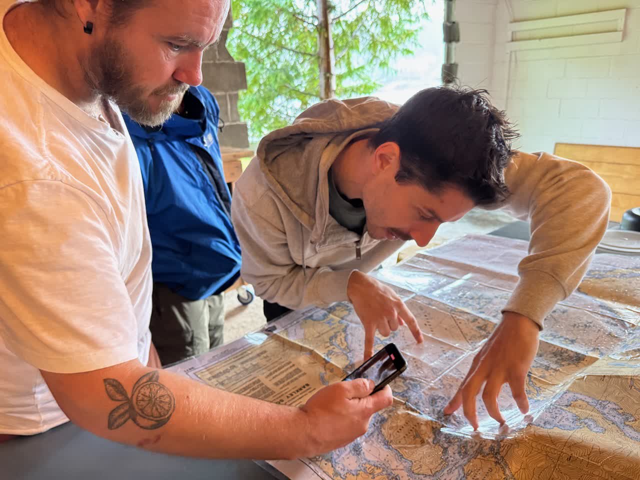 Two people leaning over a Barkley Sound marine chart, pointing at a route while one holds a phone