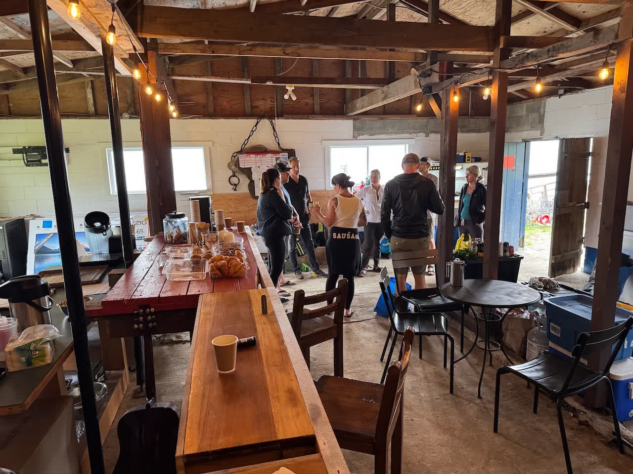 Coffee, pastries, and gear set out on the long red wooden bar in the covered staging area while paddlers chat